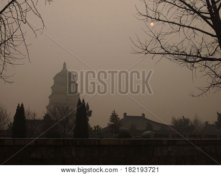 Xi'an China - Dec 23 2013: Xi'an's Landmark Big Wild-Goose Pagoda covered by heavy smog under a faintly shining sun air quality index was at the maximum of 500 points which means the air is poisonous. The smog was caused by pollution over years of industr