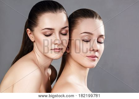 Two beautiful sensual young women with closed eyes. Over gray background.