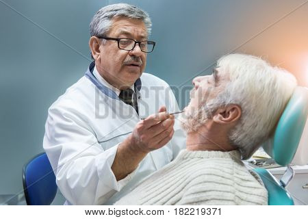 Old man at the dentist. Dental doctor is examining patient. Deep knowledge of dentistry.