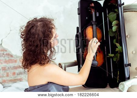 Side view beautiful womansitting near chair and touching violin in the case in studio