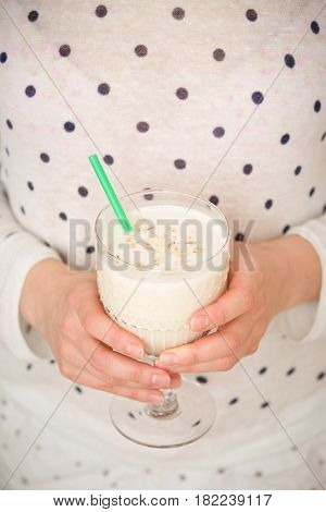 Young woman with a big glass of healthy smoothie served with a straw and oats. Hands holding milkshake. Stars background. Dairy snack or breakfast.