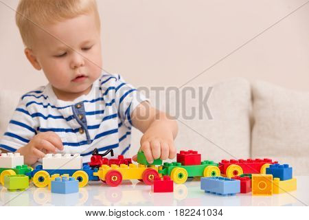 Toddler boy playing with colorful plastic bricks at the table. Toddler having fun and building out of bright constructor bricks. Early learning. stripe background. Developing toys