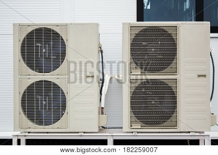 Close-up photo of two condensers of air conditioners standing on the ground in front of facade of the modern building