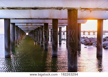 Ferroconcrete pillars of pedestrian seaside pier set in water on coast of Baltic sea. Sunset at Baltic sea in resort Palanga Lithuania. Industrial & civil architectural design in difficult conditions