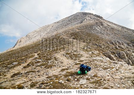 Backpack on highland mountain trail with rocky peak ahead on cloudy day