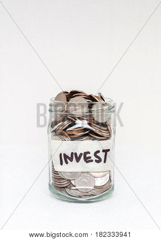 Glass jar with money and an inscription on the label `Invest` on a white background