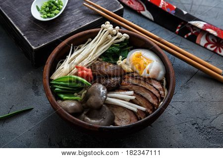 Ramen noodles bowl with egg, enoki, shiitake mushrooms, duck and onion, dark background, close view