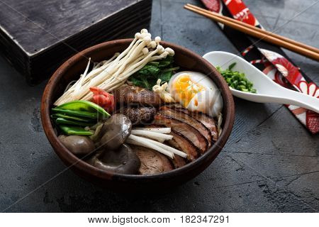 Ramen noodles bowl with egg, enoki, shiitake mushrooms, duck and onion, dark background, close view