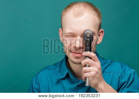 optometrist with ophthalmoscope, instrument to look into eyes by doctor on the blue background