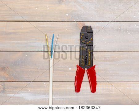 Wire stripper and wires are lying on the wooden background
