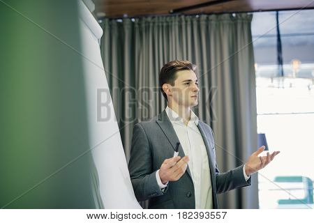 Confident Young Team Leader Or Manager Standing In Front Of A Flip Chart And Present Project On Offi