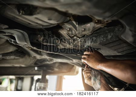 Close up of mechanic man hand at below of a car examining for change engine oil at the garage.