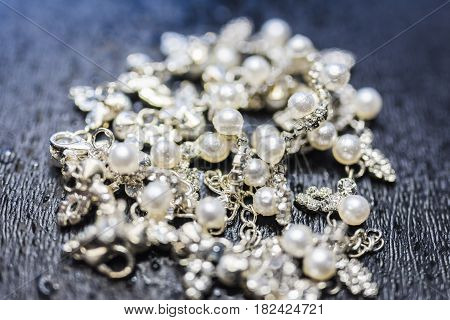Necklace of silver with pearls lying in the center of the frame on a dark background with a pronounced texture. The necklace glitters and sparkles, attracts attention