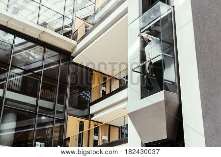 Businessman taking modern glass elevator to the upper floors