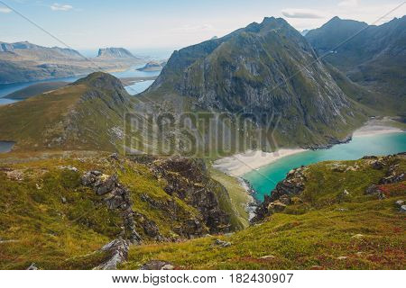 Beautiful Vibrant Norwegian Mountain Landscape from Ryten peak - famous mountain in Lofoten Islands, Moskenes municipality, Nordland with a view of Kvalvika beach, with hiking tourists and blue sky