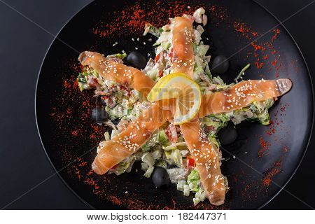 Salad with salmon vegetables and lemon on black plate and black background. Top view.