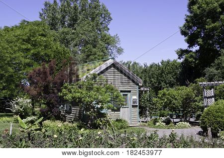 Laval, Quebec - June 14, 2015 - Landscape view of a small wooden garden house surrounded by trees foliage and a small garden in the Nature Park Laval Quebec on a sunny day in June.