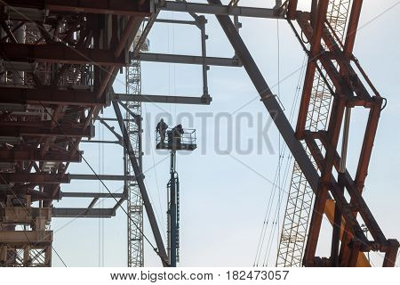 Metal scaffolding cranes and builders on the elevating work platform on the construction site.