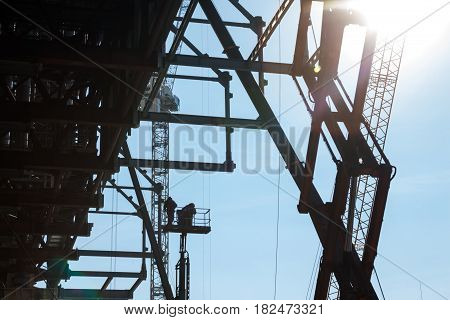Metal scaffolding cranes and builders on the elevating work platform on the construction site.