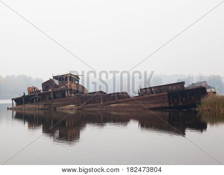 Old rusty sunken ship in water in a foggy day.