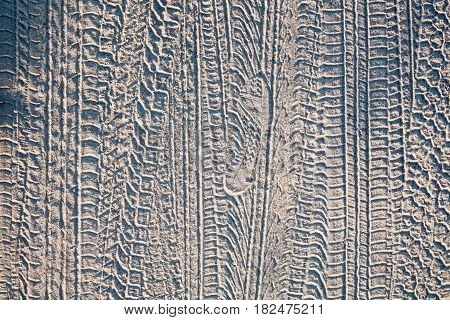 Wheel tracks and boot print on the ground on the dirt road.