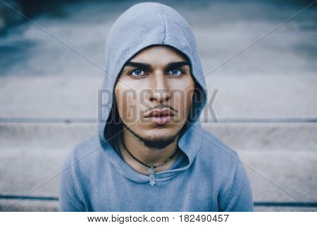 Conceptual art portrait of spooky weird beautiful handsome young middle east brunette blue eyes man face with beard wearing blue hoodie looking in camera