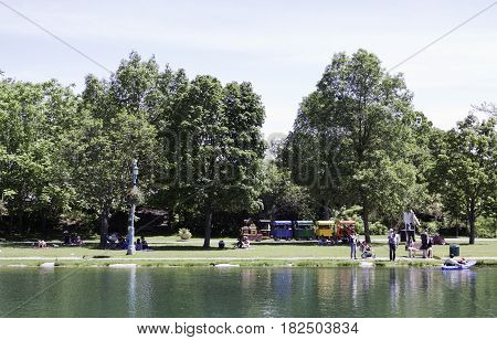 Laval, Quebec - June 14, 2015 -- Wide view of a colorful children's train ride beside a small man made lake and groups of people enjoying the weather in the Nature Park, Laval, Quebec on a sunny day in June.
