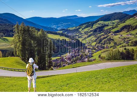 Active elderly woman-tourist with backpack photographs  at Dolomites, Tirol. Forested mountains surrounded by green Alpine meadows. The concept of ecological and active tourism