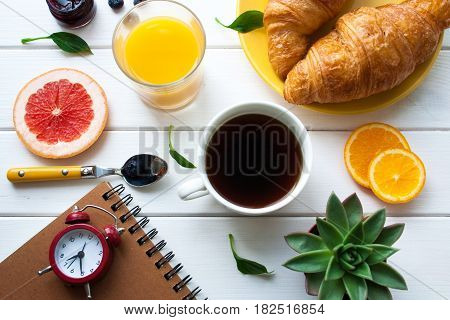 Flat lay. Breakfast with croissants a cup of coffee and an alarm clock on a wooden table