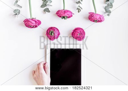 Modern spring design with bright pink flowers and tablet in hand on white desk background top view moke up