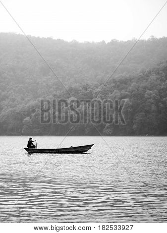 A woman alone in a canoe boat paddling on Fewa Lake Pokhara on a misty morning in black and white. Pokhara Nepal.