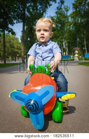Little blond kid boy driving color toy car and having fun outdoors. Child enjoying warm summer day in nature landscape