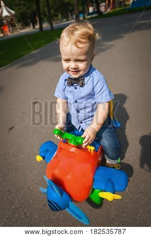 Little blond kid boy driving color toy plane and having fun in the park. Child enjoying warm summer day in nature landscape