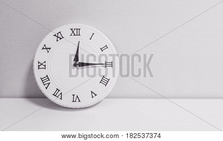 Closeup white clock for decorate show a quarter past twelve o'clock or 12:15 p.m. on white wood desk and wallpaper textured background in black and white tone with copy space