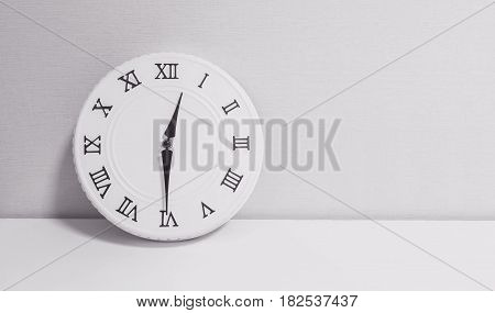 Closeup white clock for decorate show half past twelve o'clock or 12:30 p.m. on white wood desk and wallpaper textured background in black and white tone with copy space