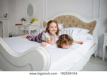 Brother and sister of primary school age play pranks on a bed. Them it is very cheerful.
