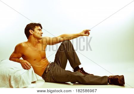 The sexy man is laying back pointing out at the sky.