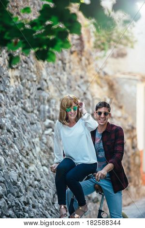 Young lovely and stylish couple un sunglasses having fun and riding bike together.