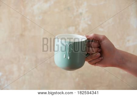 Blue cup with kefir butter milk yogurt or turkish drink ayran natural dairy product in female hand on beige wall background. Dieting and healthy eating