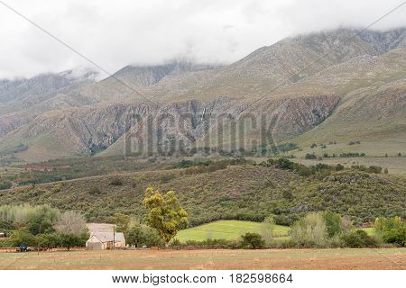 A farm landscape near Matjiesrivier with a waterfall in the back on the slopes of the cloud covered Swartberg (black mountain)