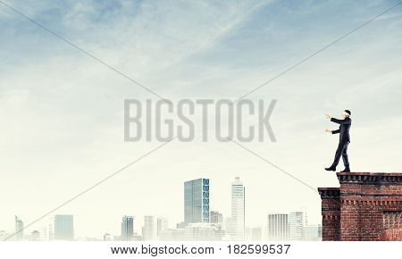Businessman with blindfolder on eyes walking on building top
