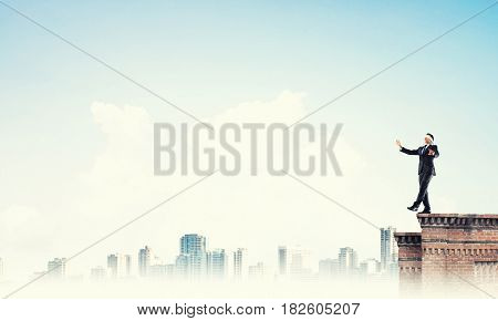 Businessman with blindfolder on eyes walking on building top