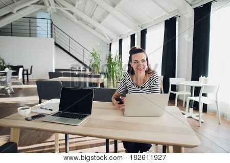 Portrait of an attractive woman sitting at the table with a laptop computer holding phone and looking away searching for inspiration for her book