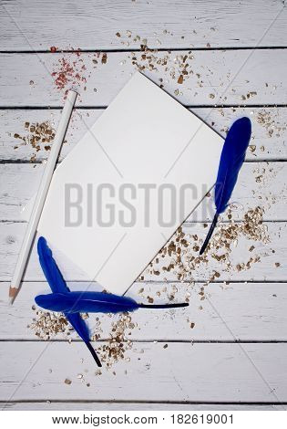 White sheet of paper with space for text withBlue feathers and gold powder. Top view. Female desktop. Rustic white table. A gentle romantic style. Diary, notebook plans for the future