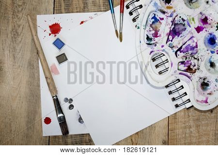 A blank sheet of paper for text surrounded by dried flower petals on a wooden background. Illustration of a hobby, drawing and inspiration. Top view.Easel, brushes, watercolor paint