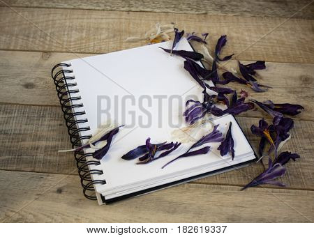 A blank sheet of paper for text surrounded by dried flower petals on a wooden background. Illustration of a hobby drawing and inspiration. Top view.Easel brushes watercolor paint