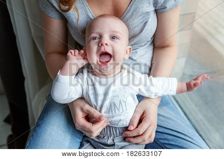 Mother holding her newborn child. Woman and new born boy relax near the windiow. Mother breast feeding baby. Family at home. Young mother playing whith her newborn son