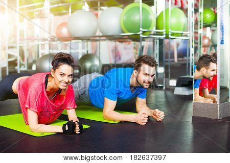 Sport - young fitness couple in  gym. Sport couple doing pushups bar on floor in the gym.