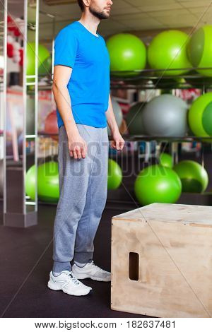 Athletic man with intense face and beard wearing a blue tee shirt performing dramatic  box jump
