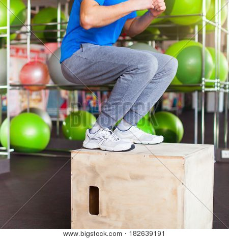 Athletic man with intense face and beard wearing a blue tee shirt performing dramatic box jump